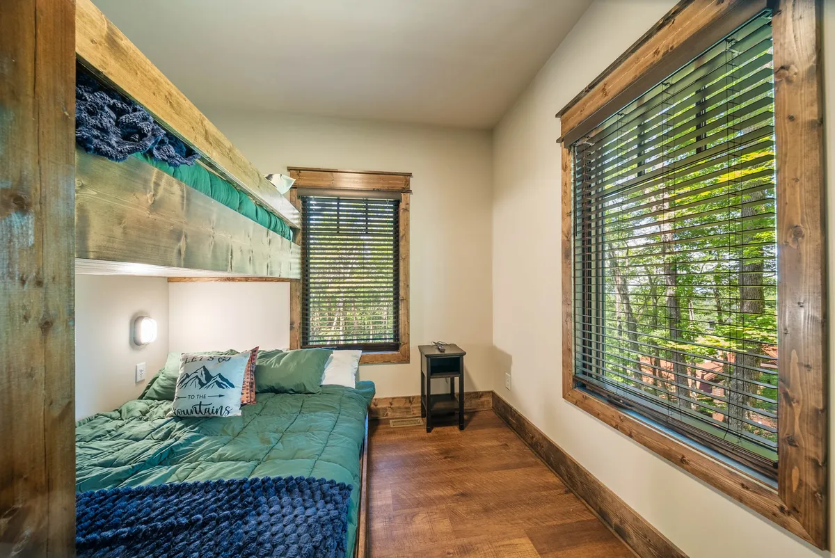 A cozy bunk room featuring a twin-over-queen bunk bed, bedside table, and windows that let in ample natural light. The inviting decor makes it especially appealing for kids or teens.