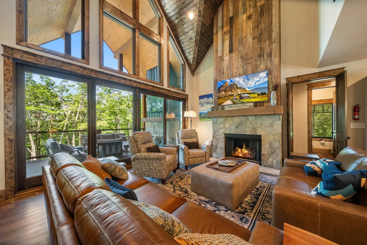 A warm, welcoming living space with large windows, a stone fireplace, and inviting seating. The room is ideal for gathering after a day on the slopes or hiking trails, creating the perfect atmosphere for making memories with loved ones.