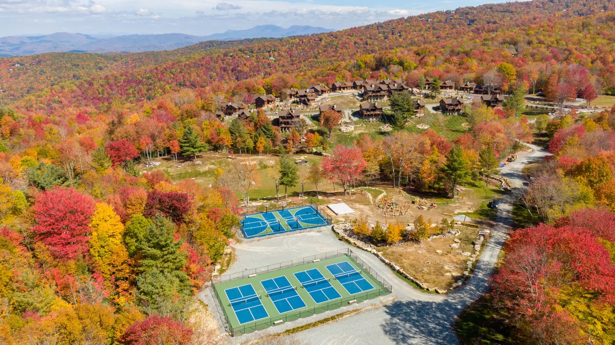 An inviting exterior showcasing colorful autumn foliage, tennis courts, residential lodges, and a dramatic mountain landscape. The scene is active yet serene, with families participating in tennis games, nature walks, and outdoor picnics, all set against the backdrop of spectacular fall colors and sunset views.