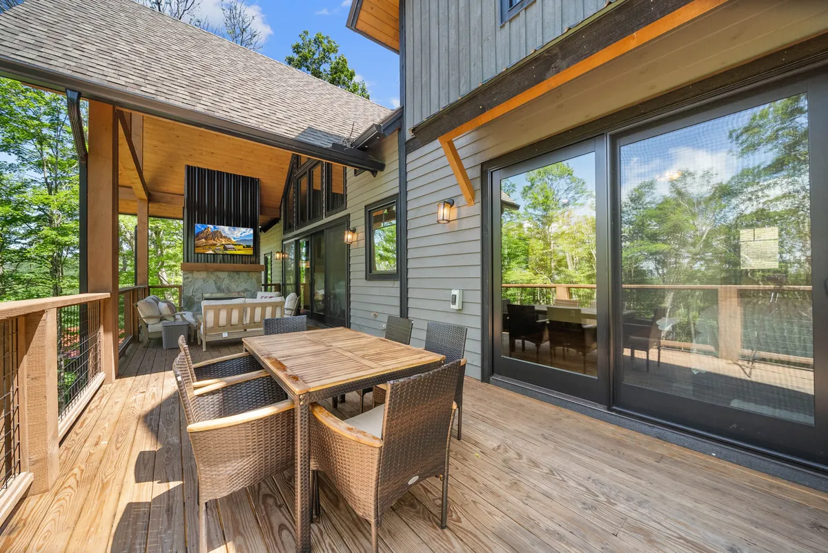 An inviting covered outdoor seating area with a wooden dining table and woven chairs, complemented by large glass doors that blur the boundaries between indoor comfort and outdoor splendor.