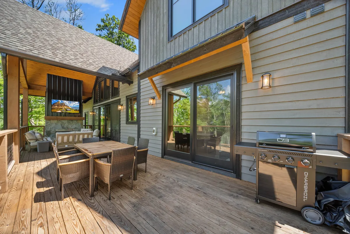 An outdoor dining area complete with a grill and comfortable seating, surrounded by greenery and large windows that connect interior and exterior spaces. The setup is ideal for group meals, celebrations, and relaxed social gatherings in the fresh mountain air.