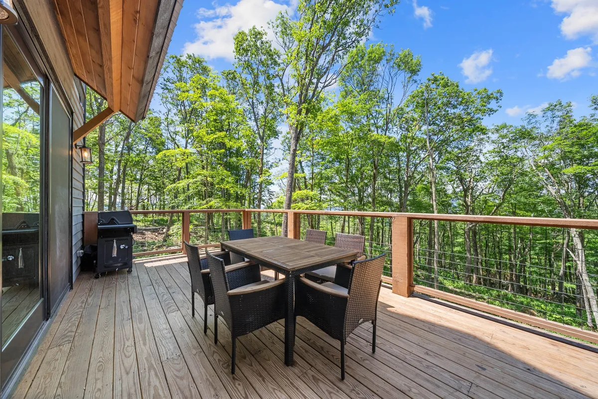 A tranquil exterior shot of a wooden deck surrounded by trees, featuring a dining table and grill ready for gatherings. The space suggests outdoor dining, barbecues, and relaxation after a day of adventure, with opportunities for stargazing and connecting privately with family in nature.