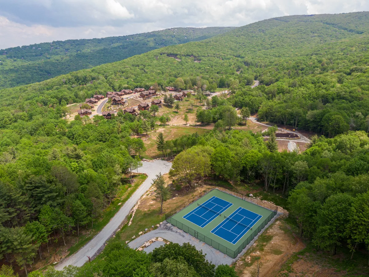 A scenic view of tennis courts framed by surrounding greenery and a mountain backdrop. A winding pathway invites exploration and the area promises active outdoor recreation, such as tennis, hiking, or simply enjoying the natural community amenities.