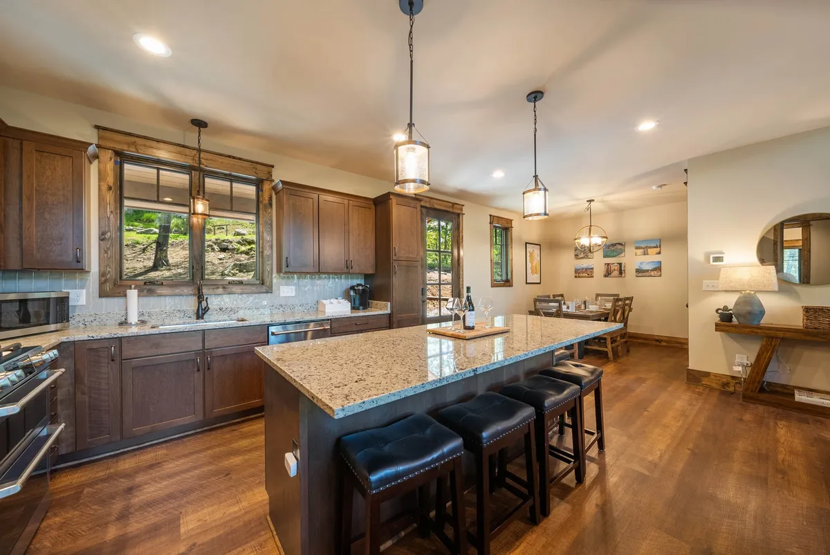 An inviting kitchen and dining area, centered around a large island with pendant lighting, wooden cabinetry, and a spacious dining table set for a meal. The layout encourages shared cooking and dining experiences, with warm lighting enhancing the welcoming mood.